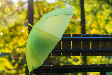 Autumn season, autumnal weather. Yellow umbrella, park wooden bench. yellow leaves blur sunlight background.