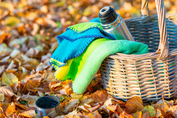 A wicker basket metal steel thermos and a cup with a hot drink, tea, coffee stands on a autumn...