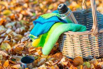 A wicker basket metal steel thermos and a cup with a hot drink, tea, coffee stands on a autumn leaves background in nature picnic autumn forest.Selective focus,blured background.