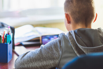 Distance learning online education. A schoolboy 10s boy studies at home and does school homework.Child sitting at table with smart phone,does remote homework.Selective soft focus blurred background.