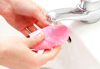 Pink facial sonic brush under faucet water, face skin care treatment - obrazy, fototapety, plakaty