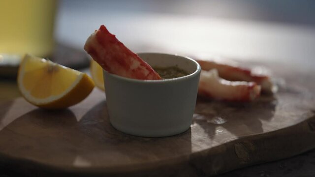 Slow motion gimbal shot of crab leg meat on a olive board with sweet lemon and dip sauce on concrete countertop