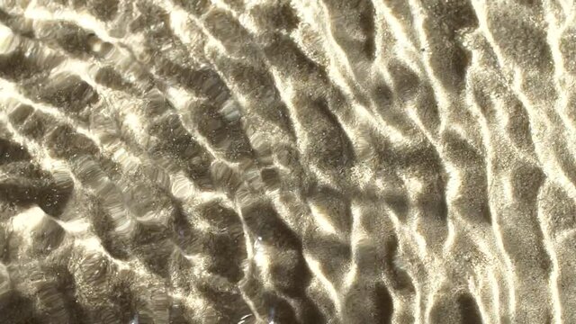 Slow motion closeup water surface texture splash and ripples on sand background