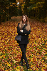 young woman with long hair and dark clothes stands on multicolored fallen leaves in the autumn forest