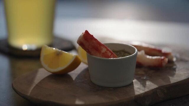Slow motion gimbal shot of crab leg meat on a olive board with sweet lemon and dip sauce on concrete countertop