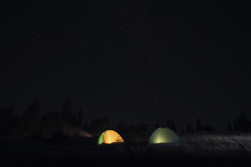 Fototapeta na wymiar Two color camping tents near forest under sky full of stars at night