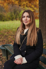 Fototapeta na wymiar close-up portrait of a young woman with long hair and dark clothes sits on a bench in the autumn forest