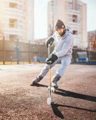 A man practicing hockey outdoors on a rubber surface in sunny weather - roller skating training -...