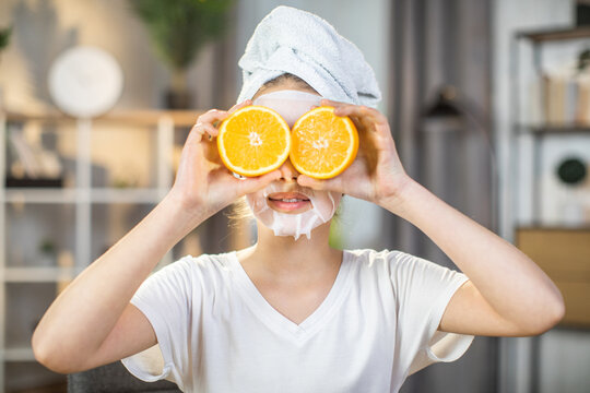 Close up portrait of pretty female teenger with towel on head and mask on face covering eyes with slices of oranges. Mineral and vitamin cosmetic for skin care at home.