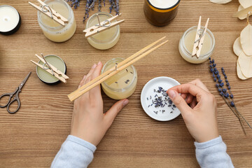 Woman making aromatic candles at wooden table, top view