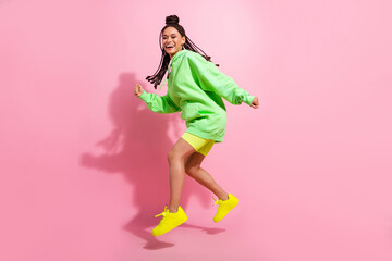 Full body photo of amazed cheerful young dark skin woman jump up go empty space isolated on pink color background