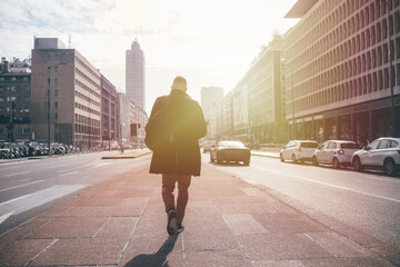 Back view young adult caucasian businessman walking away strolling city sunset