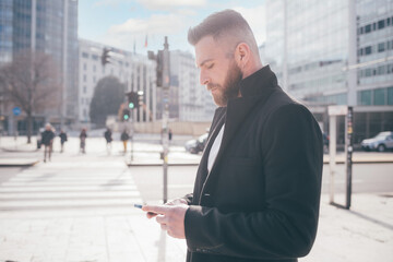 Young elegant successful adult caucasian man outdoors using smartphone browsing web remote working checking email