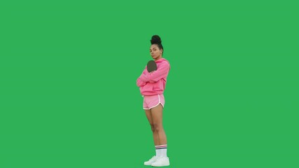 Young sporty woman table tennis player with racket over green background. Portrait of girl wearing pink hoodie and shorts looking at camera. Chroma key. 4k raw video footage - Powered by Adobe