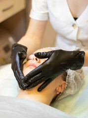 A girl beautician in a white coat, black gloves, in a medical office, cleans the problem skin of the client's face on the couch. Doctor in work environment, reception, problem skin care procedures