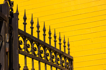 Black metal wrought iron fence against yellow brick wall. Modern exterior. Private territory,...