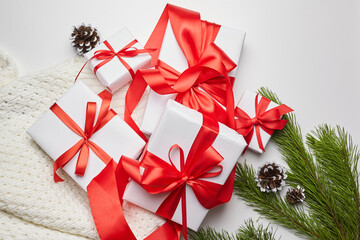 Christmas gift boxes with red ribbon and knitted sweater with green pine tree branch and cones on white