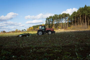 Obraz premium A farmer in a tractor, agricultural machinery, prepares the land with a cultivator. A modern red tractor in a field. Plowing a heavy tractor while cultivating agricultural work in a field with a plow.