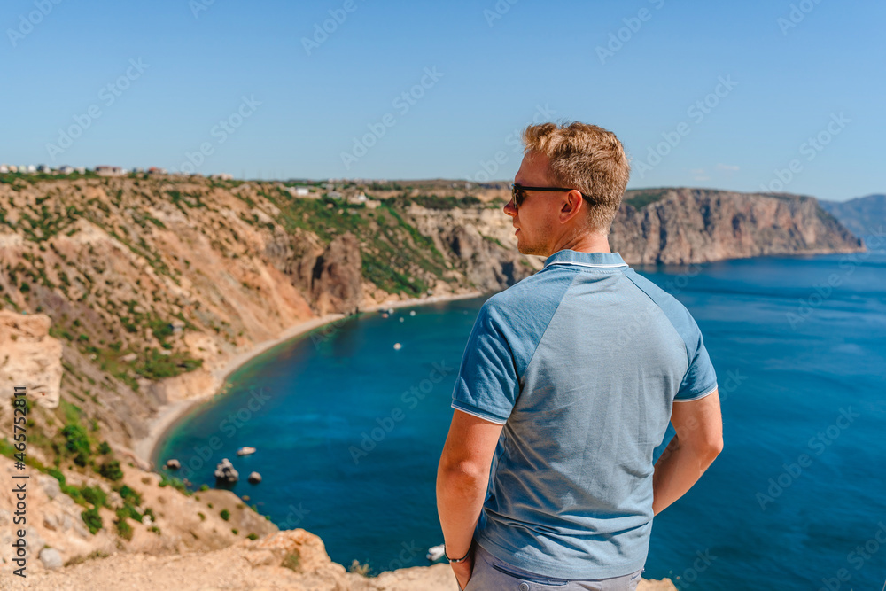 Wall mural A young man travels to Cape Fiolent, the most famous place in the Crimea with an azure wave and rocks