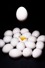 White chicken eggs with one broken egg and one in the air on a black background.