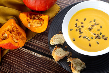 Pumpkin soup on a wooden table with other pumpkins