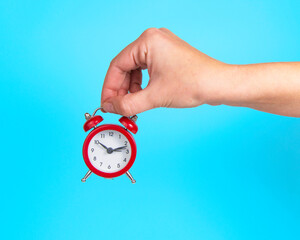 Alarm clock red color in woman hand on bright blue background
