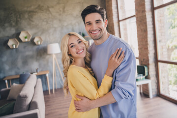 Photo of beautiful shiny young lovers dressed casual clothes hugging smiling indoors apartment