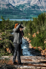 Young red-haired woman photographing mountains against the background of the river and trees