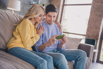 Photo of attractive sweet young couple wear casual outfits smiling sitting couch looking modern devices indoors house room