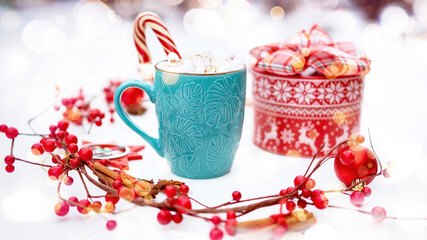 Christmas present surrounded by festive decor. A mug of hot cocoa with marshmallows and candy cane and a round gift box close-up on a white background with bokeh. Christmas giving time.