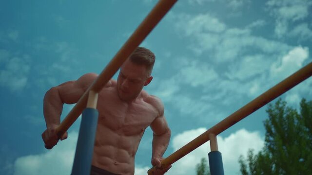 bodybuilder athlete man with perfect torso exercising dip on street in sunny day