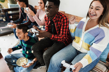 Multiracial young friends having fun playing video games at home - Focus on right girl face
