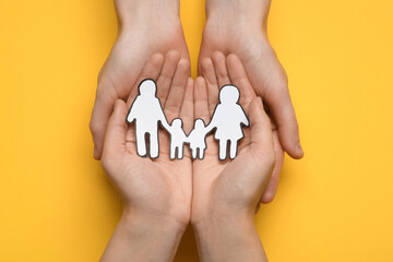 Couple holding paper family cutout on yellow background, top view