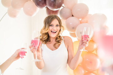 Smiling 30-year-old blonde woman holding champagne coctails at a party. Hen night, baby shower or birthday drinks with girls
