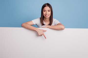 Portrait of cute promoter adviser lady direct finger down white wall billboard empty space on blue...