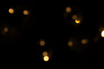 Defocused bokeh lights on black background, an abstract naturally blurred backdrop for Christmas eve or birthday party. Festive light texture. Yellow and red garland in blur. Overlay effect for design