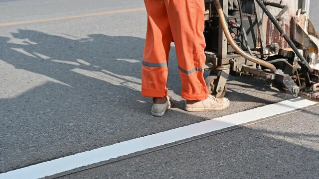 Worker wearing uniform is making the white line on road with painting machine