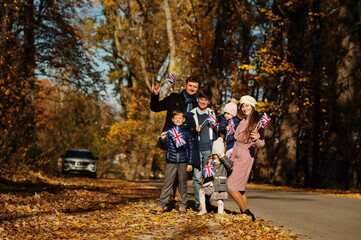 Fototapeta premium National holiday of United Kingdom. Large family with four kids holding british flags in autumn park. Britishness celebrating UK.