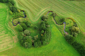 River in the wild. Aerial view of small river in middle of green field and forest in the wilderness. Natural Resource and Ecosystem. Wildlife Refuge Wetland Restoration. European Green Nature Scenery.