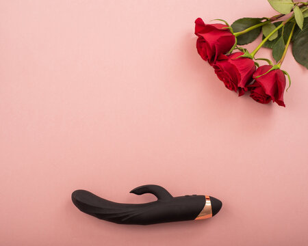 Top view of a black dildo and a bouquet of scarlet roses on a pink background. Copy space