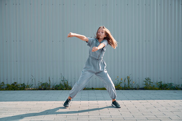 Stylish teen girl dancing hip hop outdoor on urban background. Energetic dancer performing breakdance moves