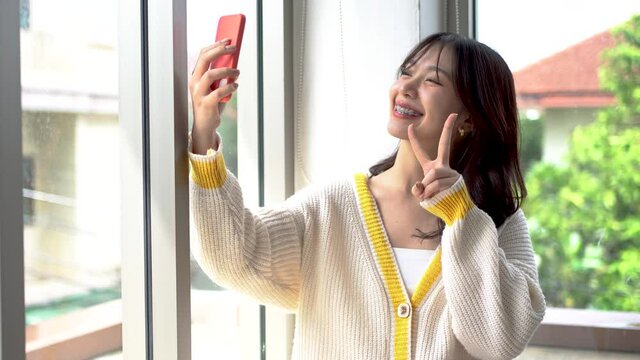 A beautiful Asian woman uses a smartphone to message friends and (selfies) take pictures of herself to post on social media.