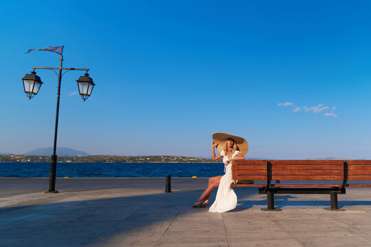 Woman in sun straw hat sitting on a wooden bench at Spetses marina, Greece