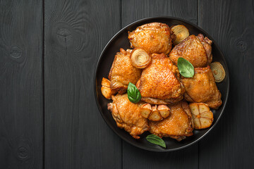 Fried chicken thighs with garlic, onion and basil in a black plate on a black background.