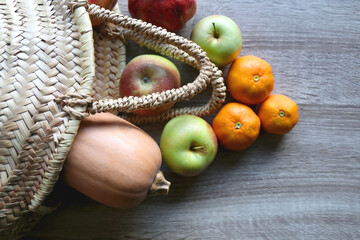 Straw tote bag filled with butternut squash and various fruit. Flat lay.
