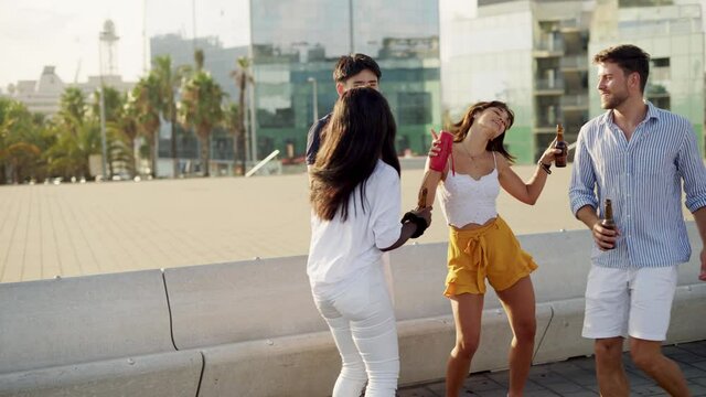 multiracial young people dancing on warm summer day outdoors, with beer bottles in hands