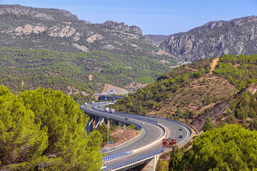 Highway winding through the Despenaperros gorge seen from a vantage point in Santa Elena. Distant features are blurred by the heath. - obrazy, fototapety, plakaty