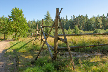 Old wooden fence with a green rustic field on a summer sunny day. Horizontal photo of pasture, animal husbandry concept