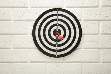 Dart Board on the white wall background. Red dart arrow hitting in the center of dartboard.