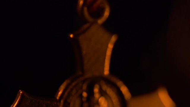 Tilt soft-focus shot of a Saint Benedict rosary with the candle burning in the background